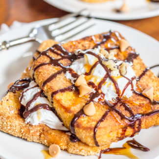 This decadent S’mores French Toast is the ideal special occasion breakfast. Soft brioche slices are dunked in a sweet vanilla milk and egg bath and then coated in graham cracker crumbs before being toasted in butter and then covered with fluff, chocolate sauce, caramel, butterscotch chips, and chopped walnuts.
