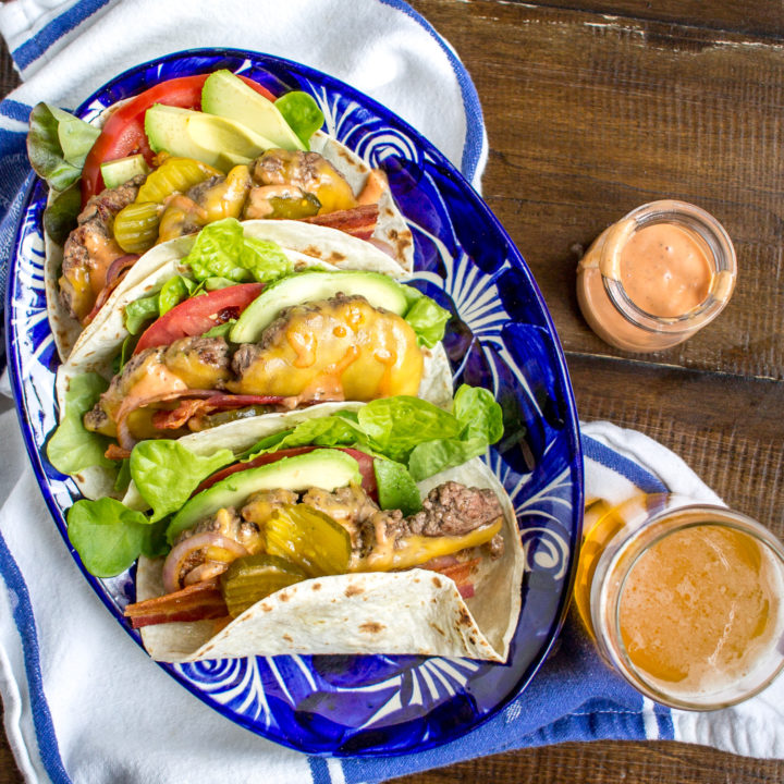 Bacon Cheeseburger Tacos are made with cheeseburger wrapped in flour tortillas and topped with tomato, avocado, bacon, lettuce, pickles, grilled red onion, and a sriracha animal sauce. They are just as crazy delicious as you might imagine.
