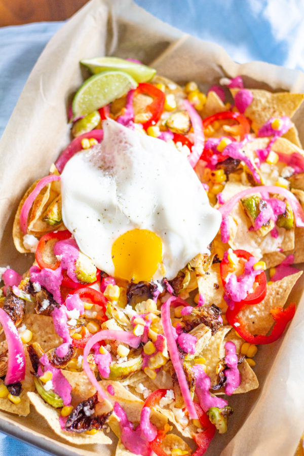 Brussels Sprout Nachos - cheesy nachos topped with roasted brussels sprouts, corn, pickled onions, fresno chilis, a fried egg, and a roasted garlic and beet crema.