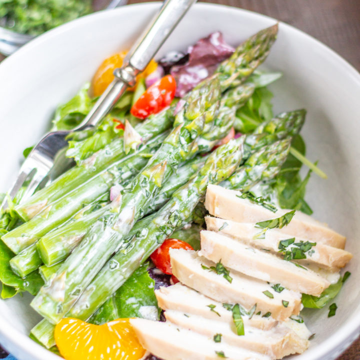 This easy to prepare Asparagus Salad is bursting with fresh flavors. Cooked asparagus, grape tomatoes, mandarin oranges, and red onion are placed on top of mixed greens and then drizzled with a light lemon tarragon yogurt dressing. Serve it as a side dish, or add chicken or salmon to turn it into a complete meal.