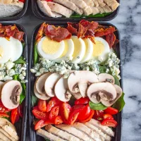 The Best Spinach Salad | A spinach salad topped with chicken breasts, tomatoes, thinly sliced mushrooms, crumbled blue cheese, hard boiled egg, and crispy prosciutto. Perfect for meal prepping.