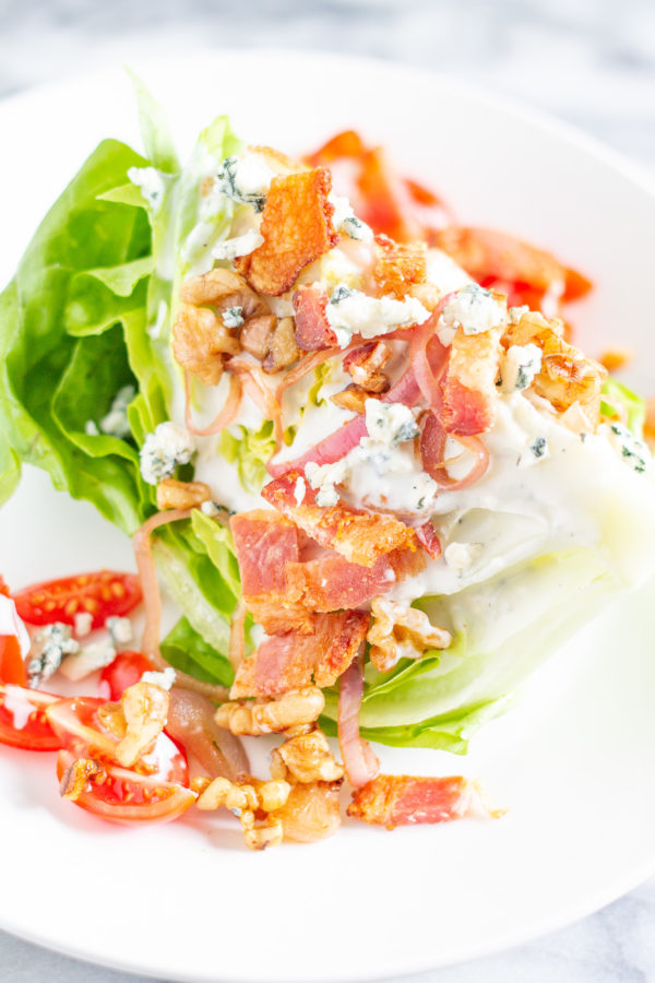 The Best Wedge Salad | A wedge salad is topped with maple toasted walnuts, thick cut bacon, grape tomatoes, caramelized shallots, and homemade chunky blue cheese dressing. 