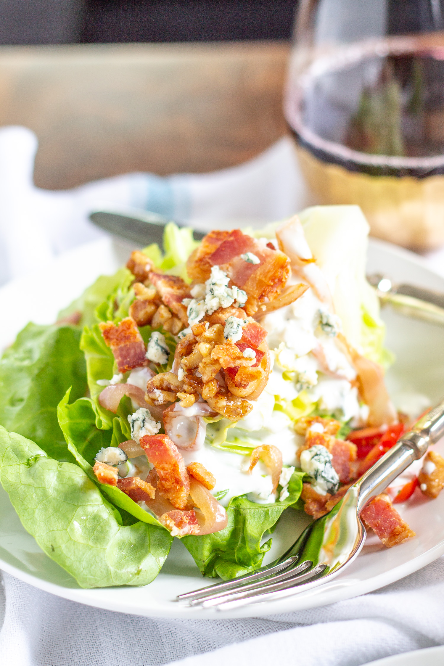 The Best Wedge Salad | A wedge salad is topped with maple toasted walnuts, thick cut bacon, grape tomatoes, caramelized shallots, and homemade chunky blue cheese dressing.