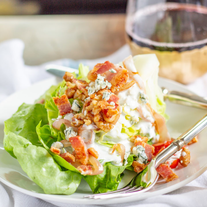 The Best Wedge Salad | A wedge salad is topped with maple toasted walnuts, thick cut bacon, grape tomatoes, caramelized shallots, and homemade chunky blue cheese dressing.