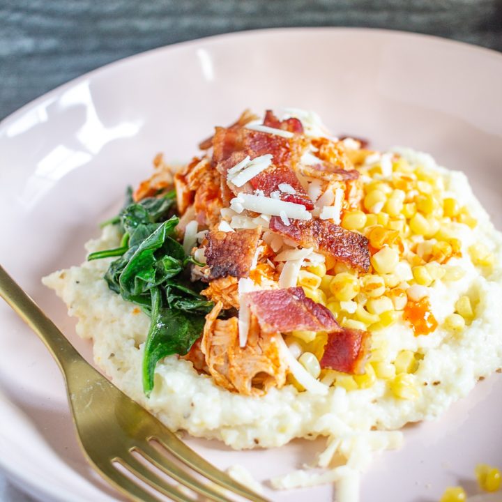 A Buffalo Chicken Grits Bowl is made with creamy cheesy grits, crispy bacon, sauteed spinach, fresh corn, and spicy shredded buffalo chicken. It's a comfort food meal that you can make in just 30 minutes.